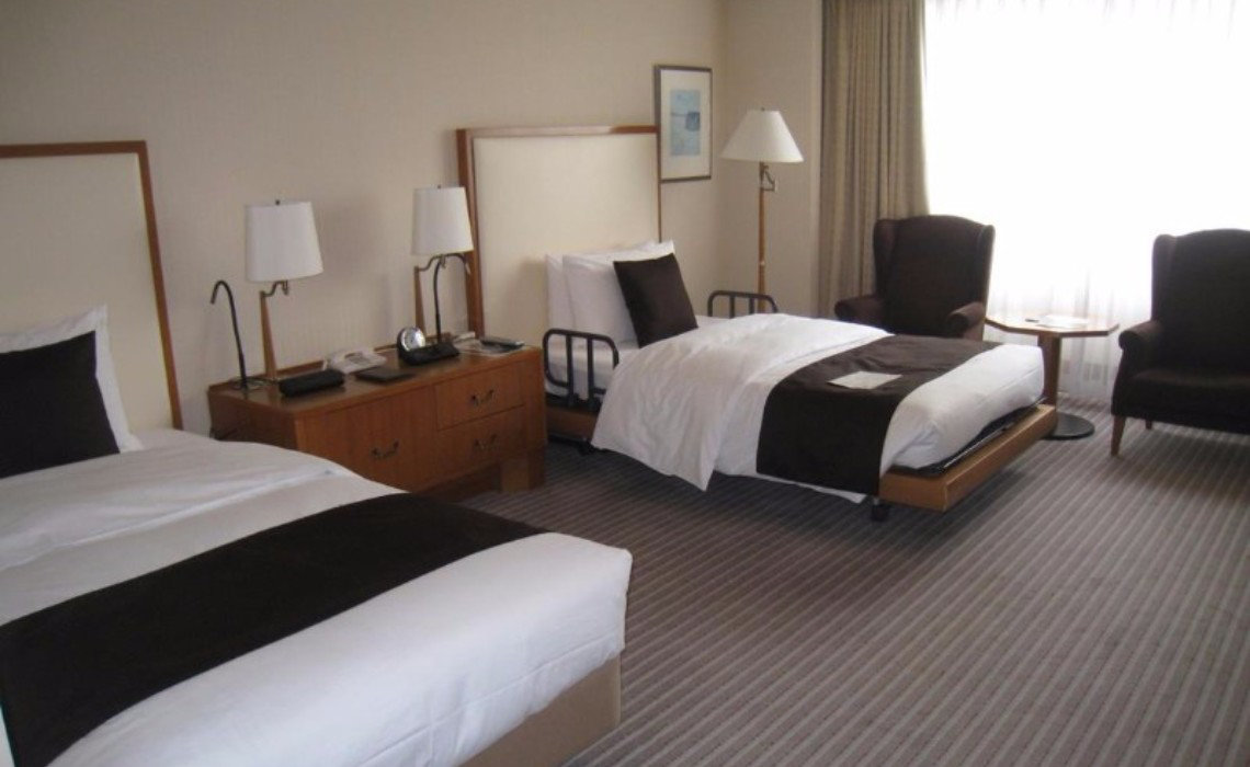 Accessible twin room at Imperial Hotel Tokyo with adjustable beds, dark chairs, and desk. Room includes a roll-in shower.