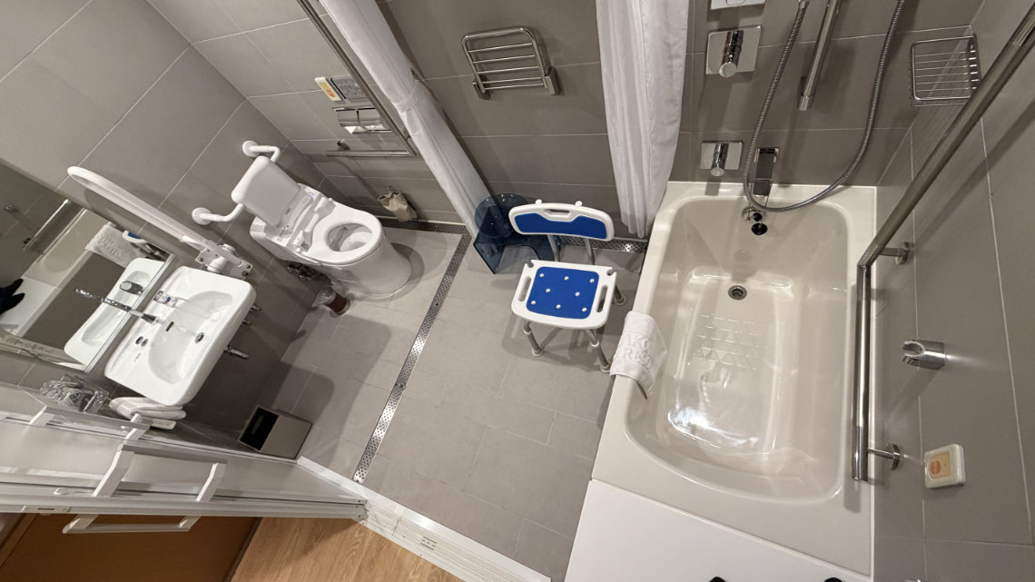 Accessible bathroom at Miyako Hotel Hakata with grab bars, shower chair, open sink, and a bathtub with handheld shower.