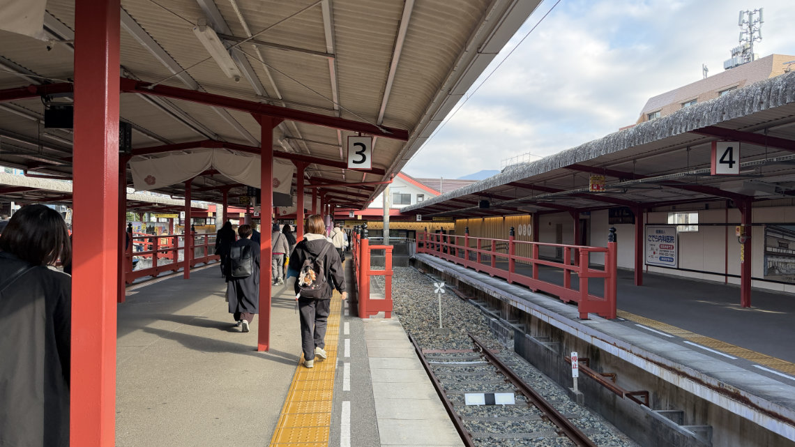 Dazaifu Station platform with red beams, tactile paving, and no platform screen doors between tracks 3 and 4.
