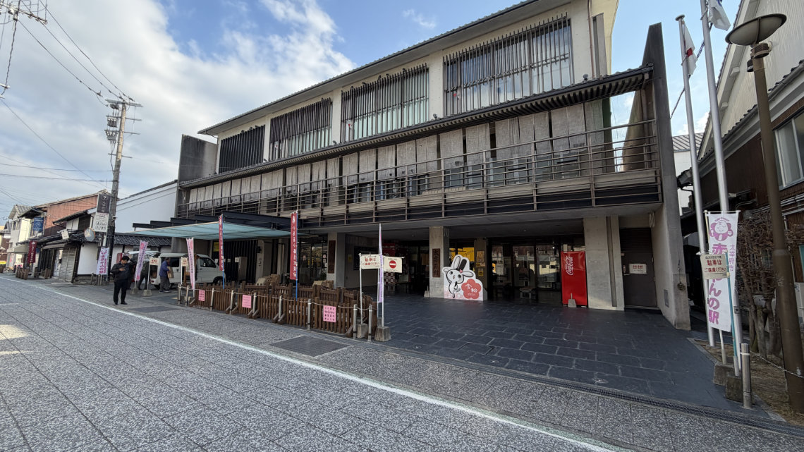 Exterior of Dazaifukan, a modern building with vending machines, signs, and an open entrance along a stone-paved shopping street.