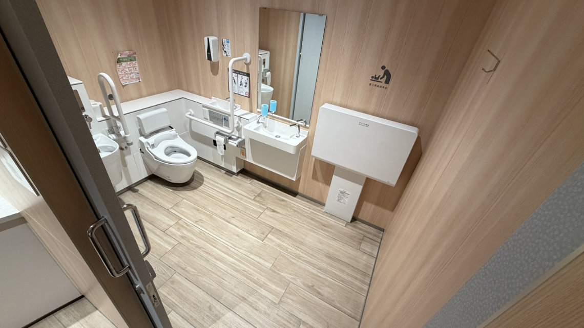 Accessible toilet at Dazaifu Tenmangu with grab bars, bidet, baby changing table, and wide sink in a clean, wood-accented space.
